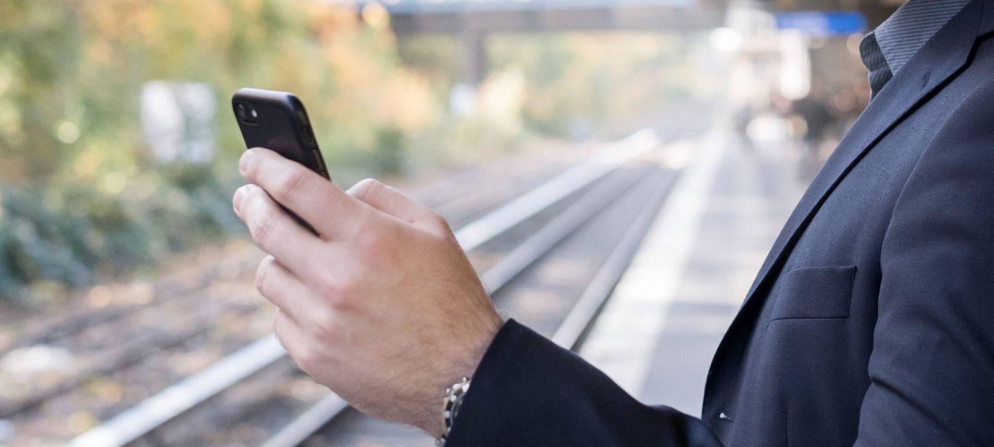 Mann mit Smartphone am Gleis