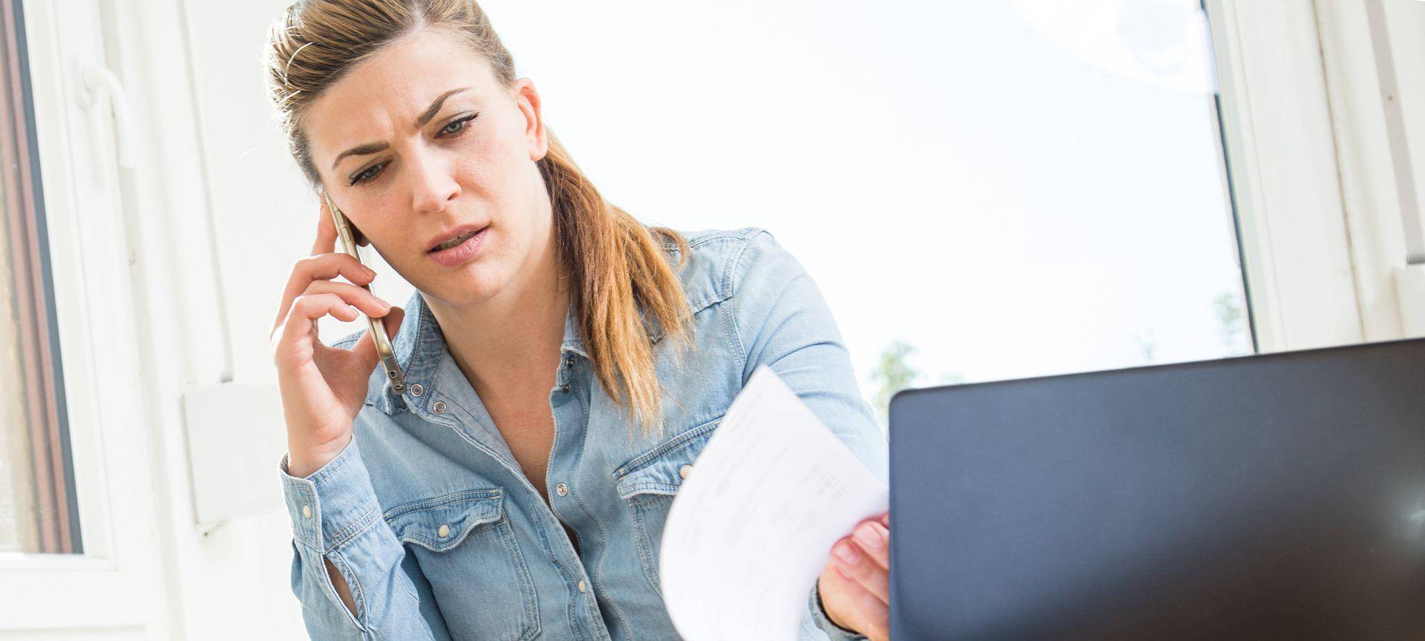 Eine Frau mit Smartphone und Laptop sichtet Unterlagen
